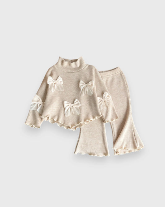 Cream baby girls' ribbed turtleneck top and flared pants with large bows and lettuce-edge trim.